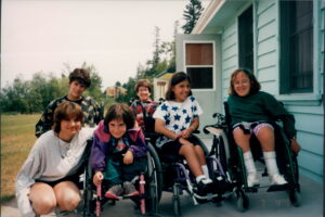 Group of youth outside on the back deck of a house. Some in wheelchairs some crouching beside.